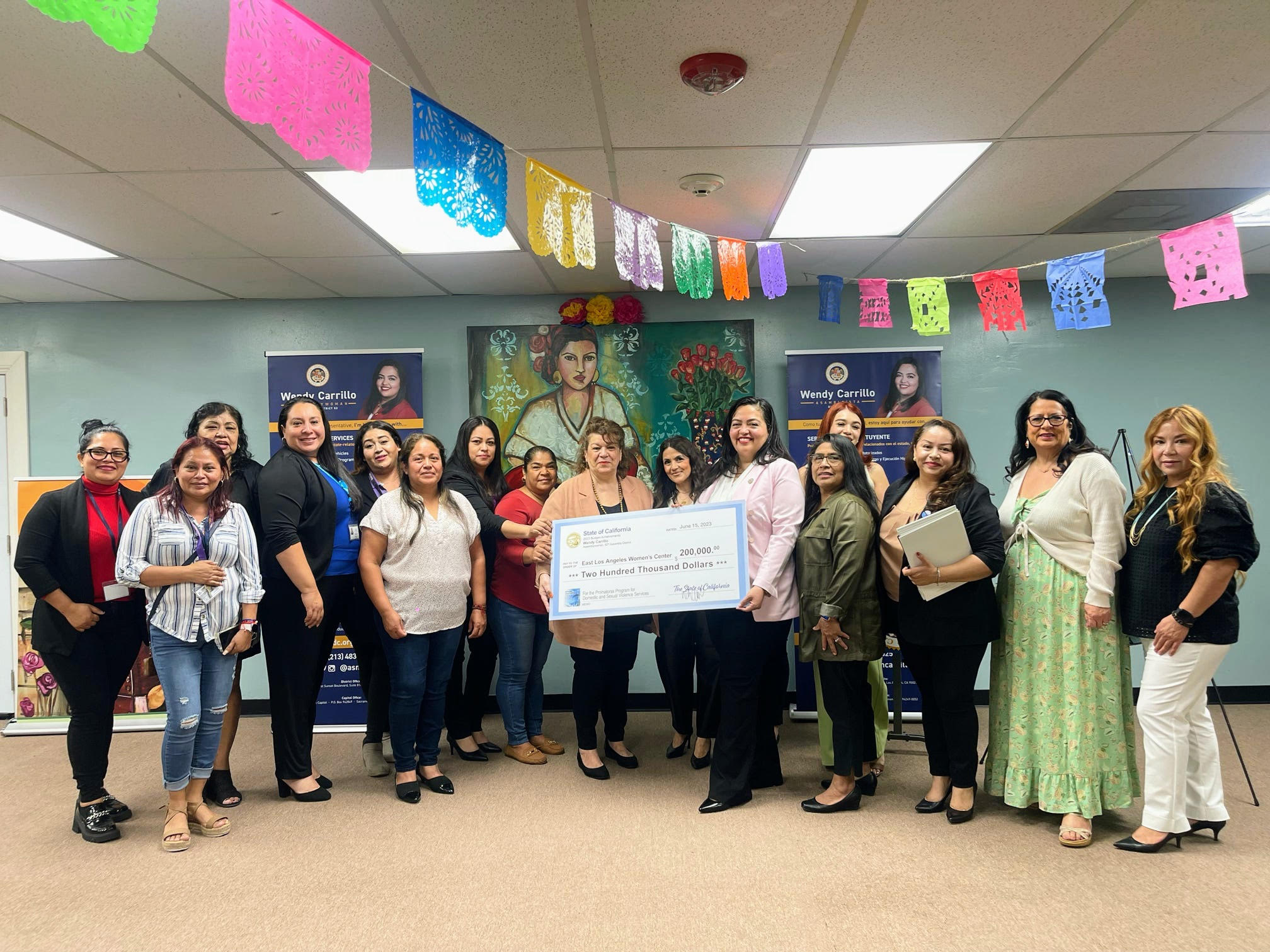 Assemblywoman Carrillo presents check to Barbara Kappos, Executive Director of East Los Angeles Women's Center, surrounded by women.