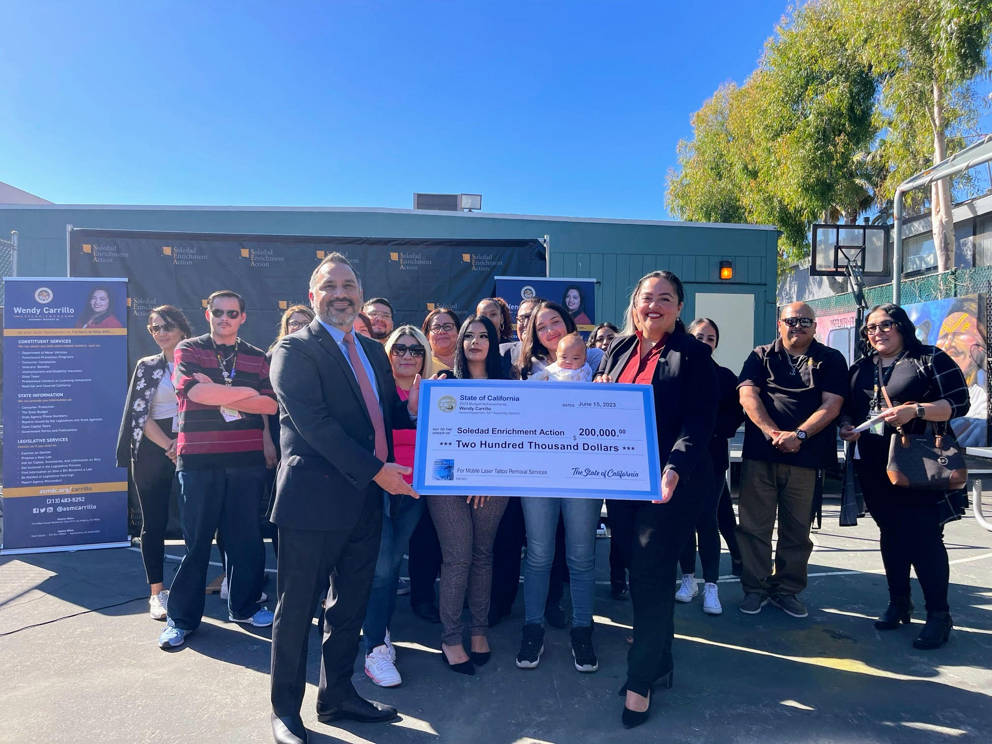 Assemblywoman Carrillo presents check to Nathan Arias, President & CEO at Soledad Enrichment Action, surrounded by other people.