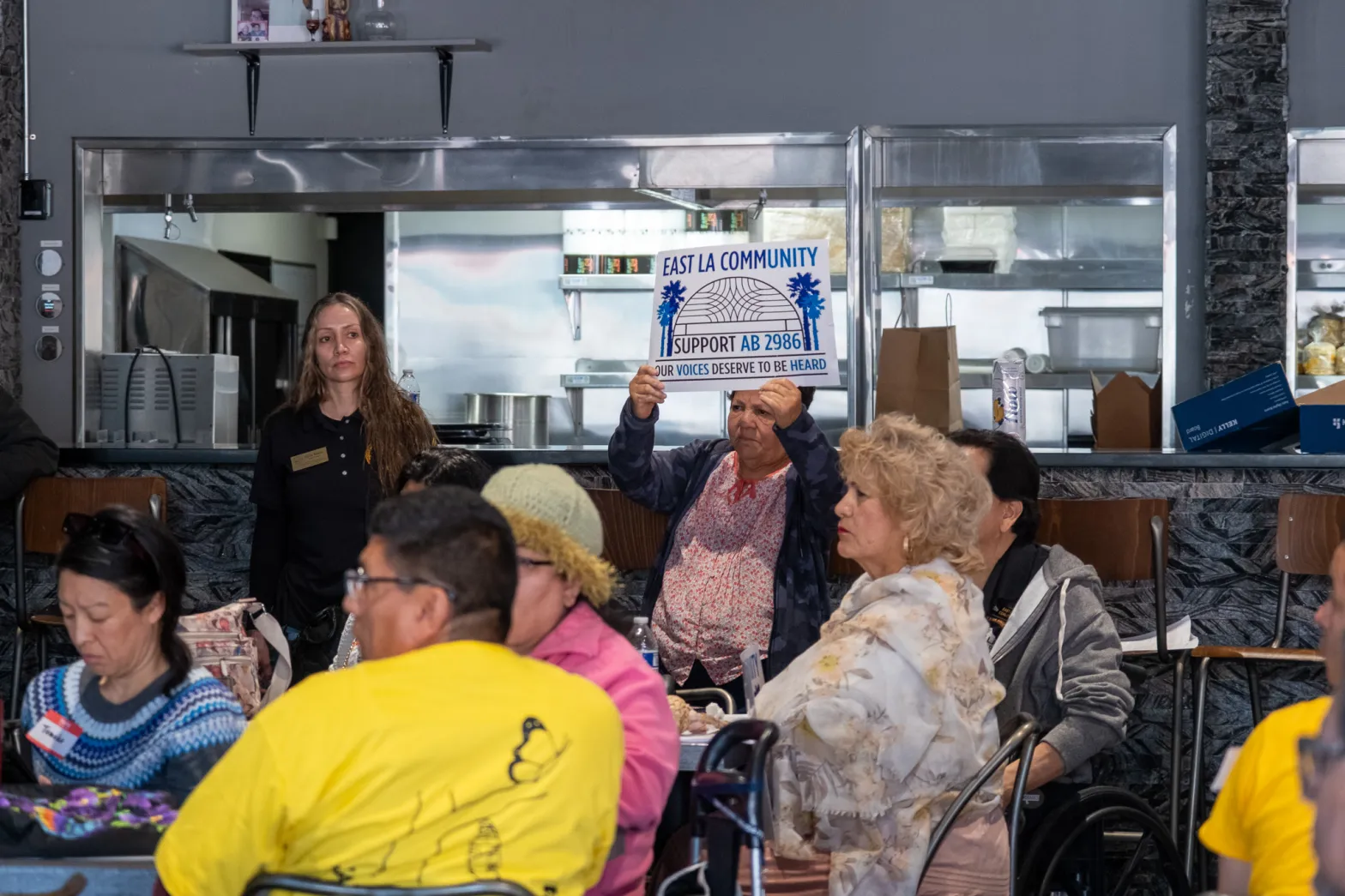 East Los Angeles resident, Maria Silvia Corona, holds a sign in favor of AB 2986 during a community meeting held at East Los Tacos on Cesar Chavez Ave on Friday, April 26, 2024.